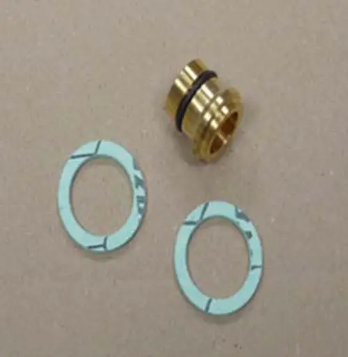 Remeha Komponenten für einen Flüssiggasumstellsatz, bestehend aus einem goldenen Anschlussstück und zwei blauen Dichtungen, auf einer neutralen Unterlage.